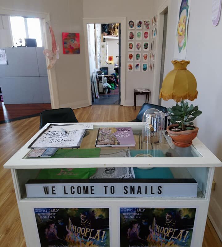 A table in the foreground with the words 'welcome to snails' in the background is the gallery with some doors.